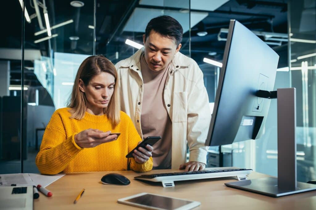 Man and woman looking at phone and computer together.